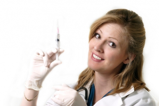 Egy doktornő ránk mosolyogva injekciós tűt tart felfelé.