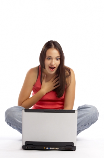 Egy fiatal lány, örömmel meglepődik a laptopja előtt ülve.