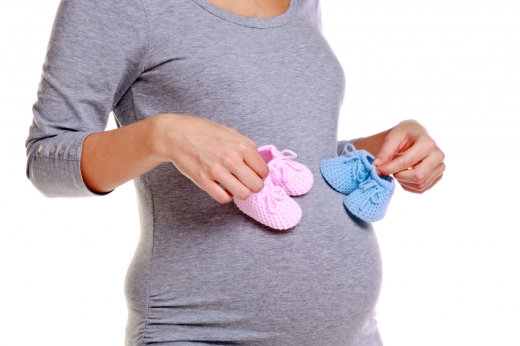 Egy terhes nő a pocakjához tart két pár bébicipőt.