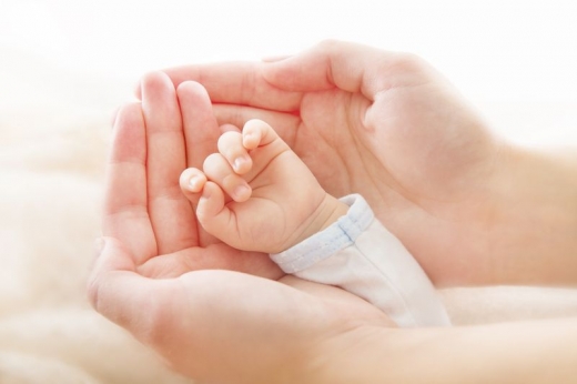 Egy anyuka két keze közé fogja kisbabája kezét.