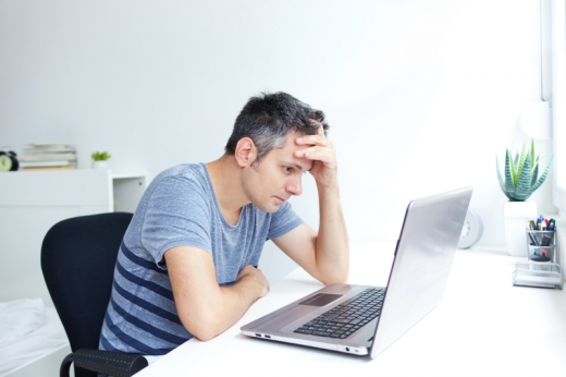 Egy férfi az irodában, az asztalánál, a laptopja előtt, könyökölve a fejét támasztja és gondterhelten nézi a laptopot.