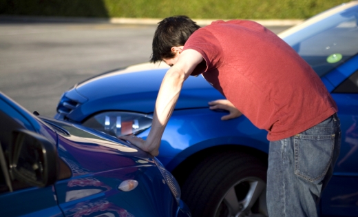 Egy férfi két kék szemben álló autóra támaszkodik.