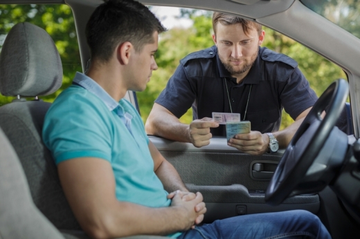 Rendőr behajol egy autóba és a fiatal sofőr jogosítványát és forgalmiját vizsgálja.