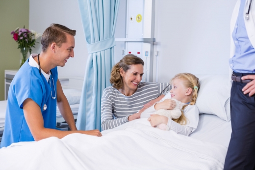 Kórházi ágynál, kislánynál a szülők és az orvos mosolyognak egymásra.