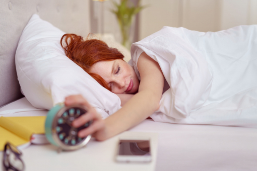 Egy fiatal nő az ágyban fekszik és kinyomja az ébresztőórát.