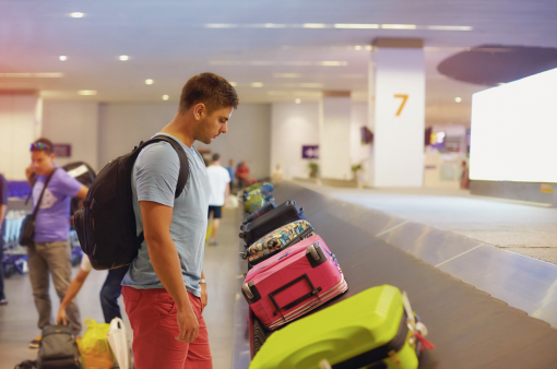 Egy fiatal férfi a reptéren a csomagját várja.